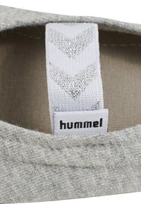 Lysegrå textil sko med en subtil glitrende tekstur, prydet med en hvid rem med metalliske chevron-detaljer og en sort "hummel"-mærkat.