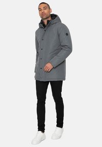 Graue, wasserdichte Jacke mit Kapuze, ausgestattet mit einem Reißverschluss und Knopfverschluss, seitlichen Taschen und einem schwarzen Akzentetikett am Ärmel.