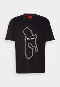 Melnas kokvilnas T-krekls ar baltu sacensību trases kontūru grafiku un vārdu "HUGO" zem tā. Apaļa kakla forma, īsas piedurknes.