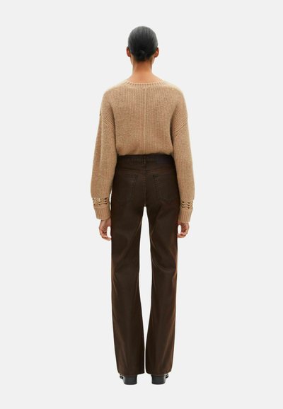 Pull en tricot beige à manches longues et texture côtelée, associé à un pantalon ample marron avec poches arrière visibles et coutures.