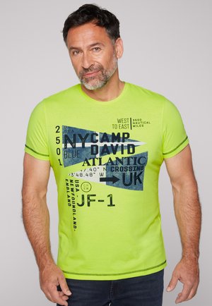 Camiseta verde neón de tela suave con estampados gráficos azules y texto, de mangas cortas y costuras contrastantes en las uniones.
