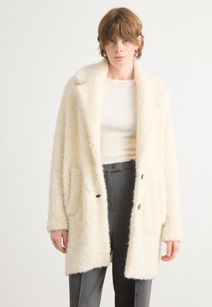 Roomkleurige, pluizige jas van textiel met een gestructureerde stof. Bevat een reverskraag, twee opgestikte zakken en donkere knopen. Draag over een lichte top.