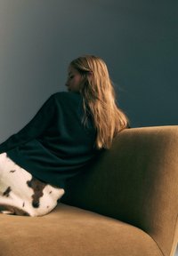 Un pull en laine noire et une couverture en peluche avec des taches marron sur un canapé beige. La scène présente une texture douce et des tons doux.
