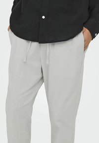 Pantalones de lino gris claro con un ajuste relajado, que cuentan con una cintura elástica y un cordón, complementados con bolsillos laterales y una textura suave.