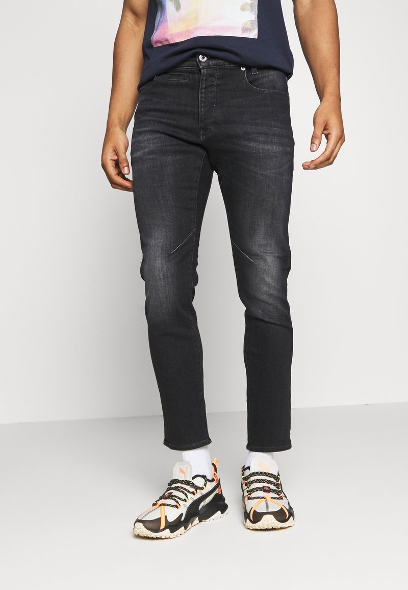 Svarta denimjeans med en åtsittande design, med subtila blekningar och distinkt sömnad. I kombination med färgglada lätta sneakers.