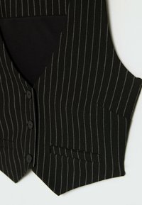 Schwarze Nadelstreifenweste mit Knopfleiste, zwei Fronttaschen und weicher Textur. Vertikale weiße Streifen bilden einen Kontrast zum dunklen Stoff.