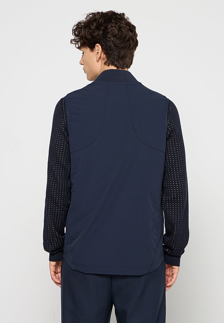 Gilet navy avec une texture lisse, présentant un col classique, des coutures au dos et des manches longues à motif dans une couleur contrastante.