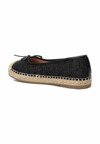 Zapato negro de trama con punta redondeada, con suela de yute y un lazo negro en la parte frontal. Ribete de cuero suave.