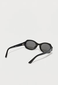 Gafas de sol negras con un diseño elegante y redondeado, que cuentan con lentes oscuros y brazos largos y curvados. Decoradas con un sutil logotipo en uno de los brazos.