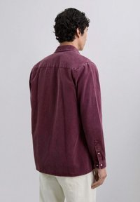 Bordowa koszula zapinana na guziki z kołnierzykiem, długimi rękawami i luźnym krojem. Gładka faktura z widocznymi szwami i guzikami.