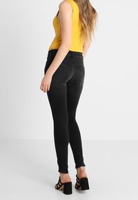 Jeans negros ajustados con una textura suave y un diseño entallado. Presentan un ligero deshilachado en el dobladillo y una cintura de altura media.