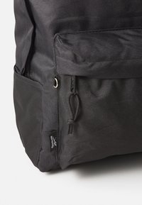 Schwarzer Stoff-Rucksack mit texturiertem Finish, ausgestattet mit einer Fronttasche und Kordelzugverschluss, sowie einem Markenetikett an der Seite.