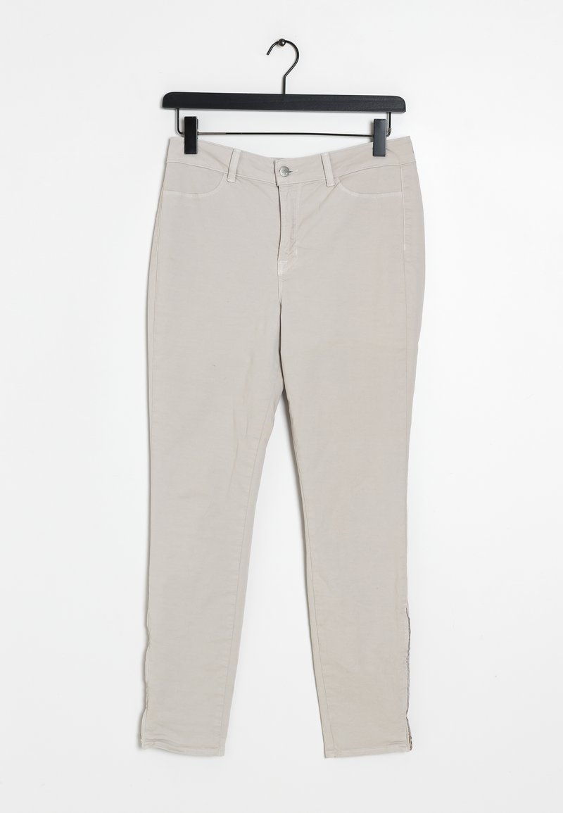 Beige, slim-fit pants made of cotton with a smooth texture. Features front pockets and a zipper fly with a button closure. Hanging from a black hook.