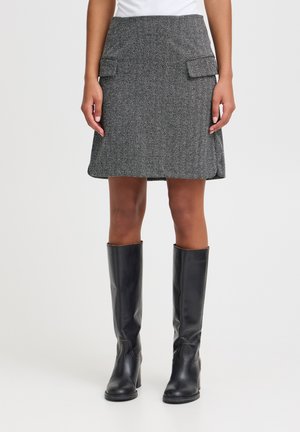 Jupe en mélange de laine grise avec un motif en chevrons, deux poches avant et une coupe évasée ; portée avec des bottes en cuir noir brillant jusqu'au genou.