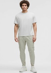 Camiseta corta de manga gris claro combinada con pantalones cargo beige con bolsillos, complementados por zapatillas blancas. Tejido suave, corte relajado.