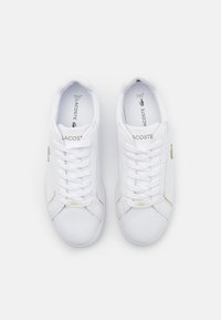 Vita lädersneakers med rund tå, snörningsdesign, subtila gulddetaljer och Lacoste-logotyp på tungan och sidopanelen.