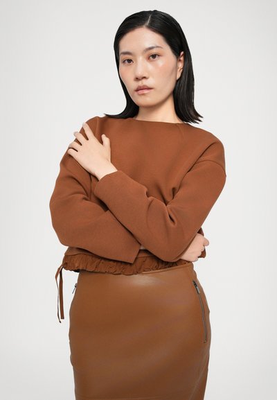 Hnědá zkrácená mikina s texturovaným volánem na spodním lemu, spárovaná s upnutou hnědou sukní z umělé kůže s bočním zipem.