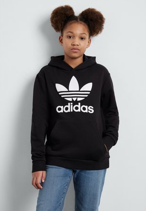 Black hooded sweatshirt with a large white Adidas logo and three stripe design on the chest. Front kangaroo pocket, set against a light background.