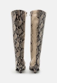 Paired bottes hautes jusqu'au genou avec un motif de peau de serpent noir et beige, talons bas effilés, et fermetures éclair latérales sur fond blanc uni.