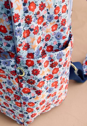 Vrecko na batoh z látky s kvetinovým vzorom, červenými a fialovými kvetmi, béžovými hviezdami a modrým popruhom na béžovom pozadí.