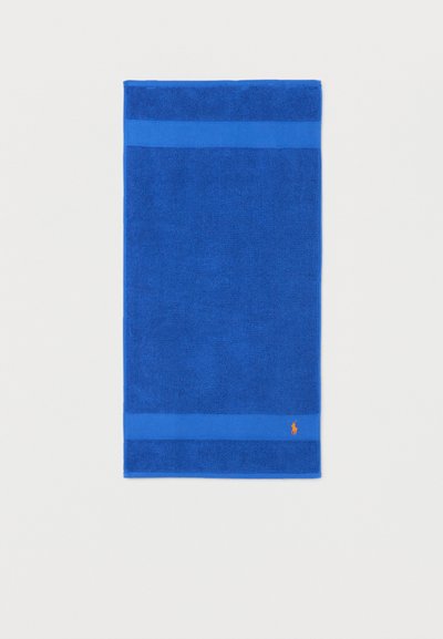 Μπλε ορθογώνια πετσέτα με υφασμάτινη υφή και λείες άκρες, με μικρό πορτοκαλί κεντημένο λογότυπο κοντά σε μία γωνία.
