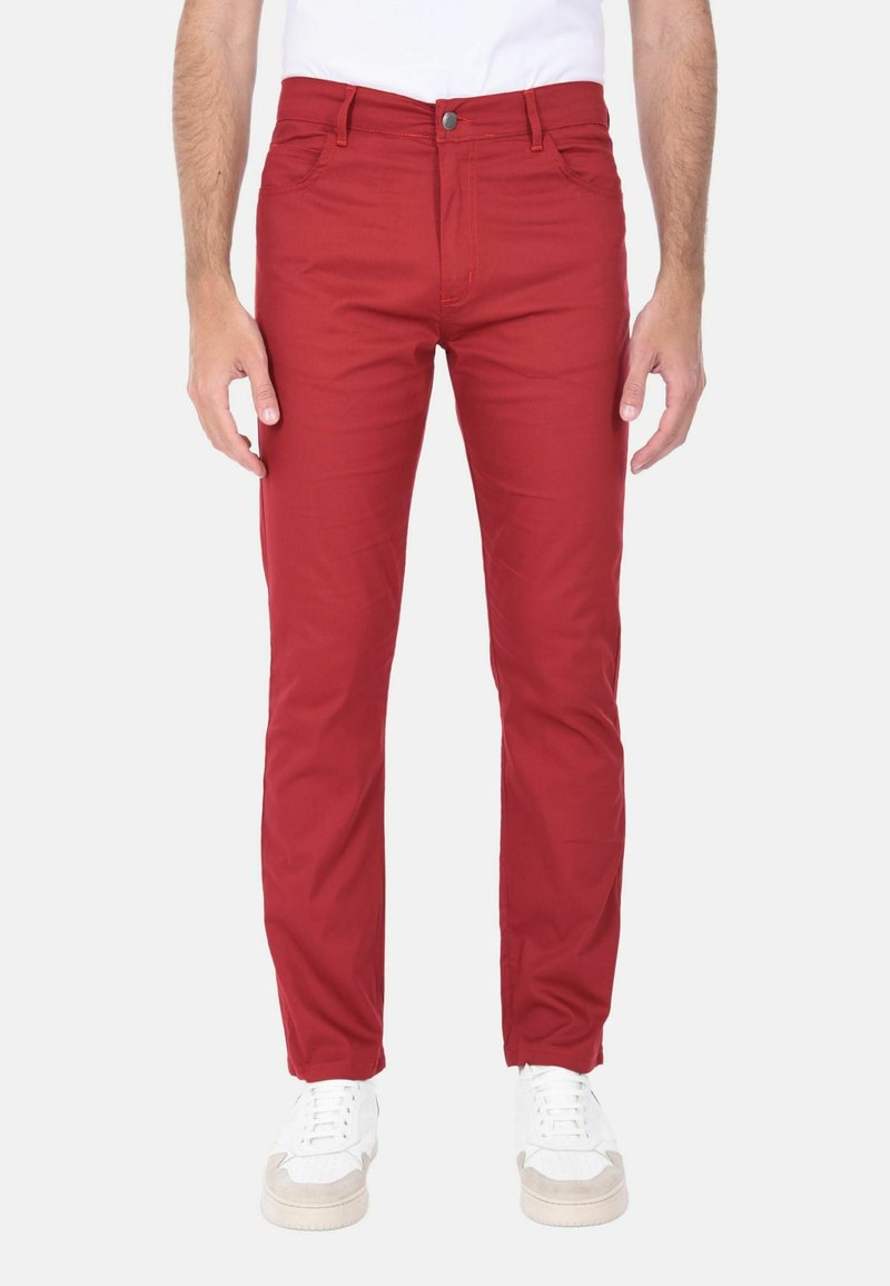 Pantaloni di cotone rossi a vestibilità slim, con cinque tasche, chiusura a bottone e dettagli di cucitura a contrasto, abbinati a scarpe bianche.