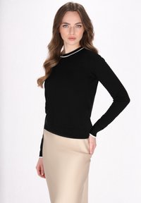 Maglione nero a maniche lunghe in maglia con dettaglio bianco sul colletto, abbinato a un gonnella di satin beige, esposto su uno sfondo bianco.