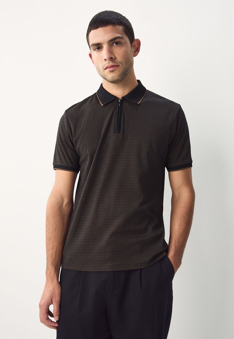 Zwart poloshirt met een ziphals, voorzien van een textuurpatroon en een contrasterende kraag. Korte mouwen en een slanke pasvorm.