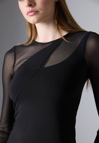 Maglietta nera a maniche lunghe con una combinazione di tessuto opaco e trasparente, caratterizzata da un design geometrico sul petto e una texture liscia.
