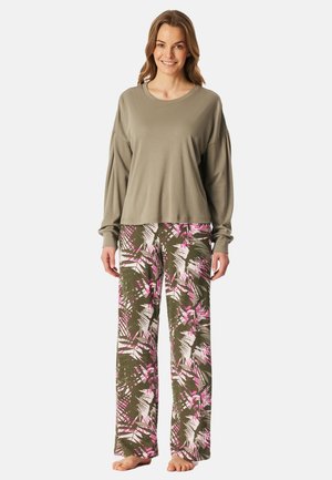 Grå langærmet top parret med løstsiddende grønne pyjamasbukser med et pink og hvidt abstrakt mønster, barfodet på en ensfarvet baggrund.