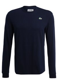 Camiseta de manga larga azul marino hecha de algodón. Presenta un pequeño logo de cocodrilo verde de Lacoste en el pecho. Diseño clásico de cuello redondo.