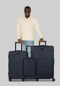 Conjunto de equipaje rígido en color azul marino que incluye una maleta grande, una maleta mediana y una maleta de mano, con texturas suaves y asas retráctiles.