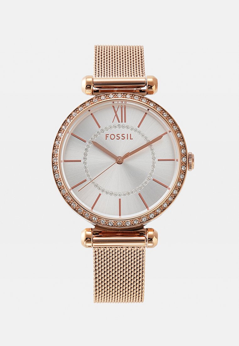 Złoty różowy zegarek na siateczkowym pasku z srebrną tarczą. Posiada bezel zdobiony kryształami, rzymską cyfrę XII oraz różowo-złote znaczniki godzin.
