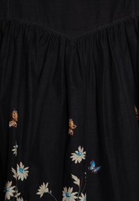 Vestido de tecido preto com textura franzida e bordados florais com borboletas em tons de amarelo, azul e creme na bainha.