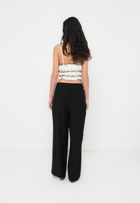 Haut court blanc avec bords volantés et bordure noire, associé à un pantalon noir ample avec une taille élastique et des jambes larges.