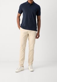 Marineblauwe polo-shirt, korte mouwen, met een placket van twee knopen; gecombineerd met crème kleurige chinos en witte sneakers. Eenvoudige, klassieke pasvorm en ontwerp.
