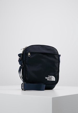 Kompaktowa, granatowa torba na ramię z regulowanym paskiem i przednią kieszenią na suwak, z białym logo The North Face.