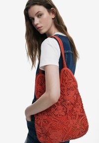 Red crochet bag with floral design, textured weave, and dual handles. The bag features a spacious, open structure.