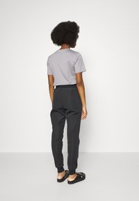 Gray short-sleeve t-shirt and black jogger pants with elastic waistband, featuring a back pocket and logo detail. Black sandals complete the look.