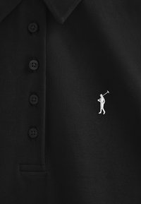 Camiseta polo negra hecha de tela texturizada con una tapeta de tres botones. Logo de golfista bordado en blanco en el lado izquierdo del pecho.