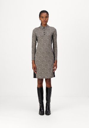 Leopardenmusterkleid mit langen Ärmeln, Kragen, seitlichen Schlitzen und kontrastierendem schwarzen Detail. Kombiniert mit knielangen schwarzen Stiefeln.