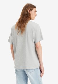 Camiseta gris de manga corta hecha de algodón. Corte relajado con cuello redondo y costura visible. Llevada con jeans de color azul claro.