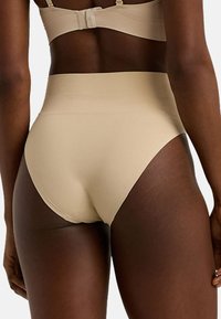 Höga beige underkläder med en mjuk, elastisk textur och sömlösa kanter. Har en bred midjeband för komfort och stöd.