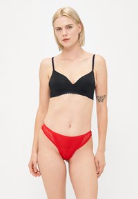 Reggiseno wireless nero con bordo ondulato, abbinato a uno slip in pizzo rosso con motivo geometrico e fascia elastica.