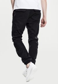 Pantalones jogger negros hechos de una mezcla de algodón, con puños elásticos, bolsillos laterales y un corte relajado. Combinados con zapatillas blancas.