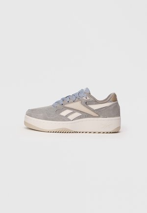 Grå ruskind og beige atletik-sneaker med lyseblå snørebånd og tyk hvid sål, vist fra siden på en ensfarvet baggrund.