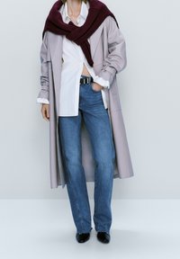 Trench coat di un leggero lavanda sopra una camicia bianca, jeans blu dritti e stivali neri a punta. Scialle in maglia bordeaux attorno al collo.