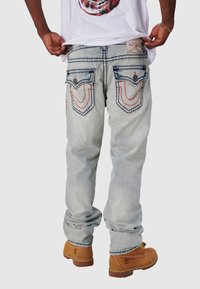 Jasnoniebieskie dżinsy o luźnym kroju, z pomarańczowym i niebieskim przeszyciem na tylnej kieszeni oraz skórzaną metką na pasku.