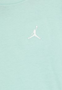Bleda zelena bombažna majica s stikano belo Jumpman logotipom na levi prsni strani, z gladko teksturo in okroglim izrezom.
