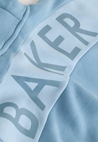 Hellblauer Pullover mit großem, erhabenem Schriftzug "BAKER" in Grau. Weiche Textur mit rundem Kapuzen-Einsatz und Nähtendetails.